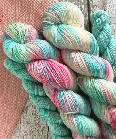 Colorful yarn skeins on a wooden surface with a pink fabric background.